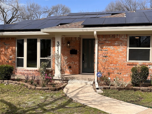 entrance to property featuring covered porch, a shingled roof, and brick siding