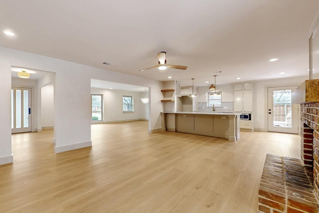 kitchen featuring a fireplace, light wood-style floors, open floor plan, white cabinets, and stainless steel microwave