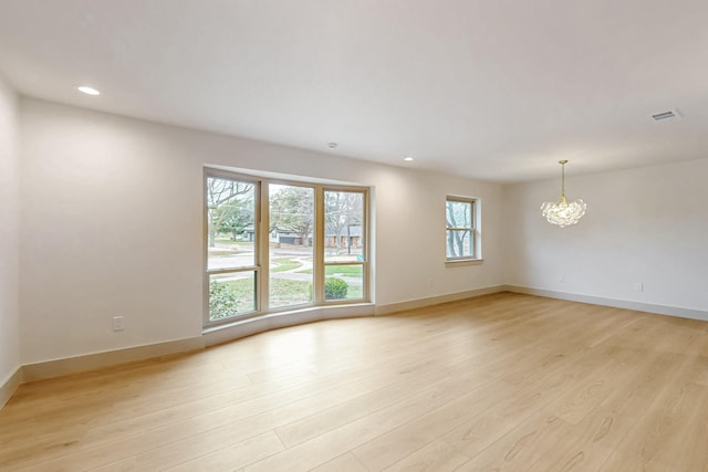 empty room with visible vents, a notable chandelier, light wood-style flooring, and baseboards