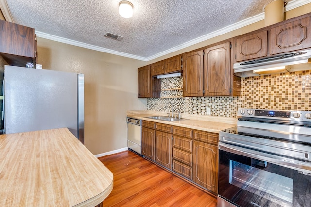 kitchen featuring crown molding, light countertops, appliances with stainless steel finishes, a sink, and under cabinet range hood