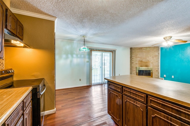 kitchen with under cabinet range hood, electric stove, ornamental molding, a brick fireplace, and dark wood-style floors