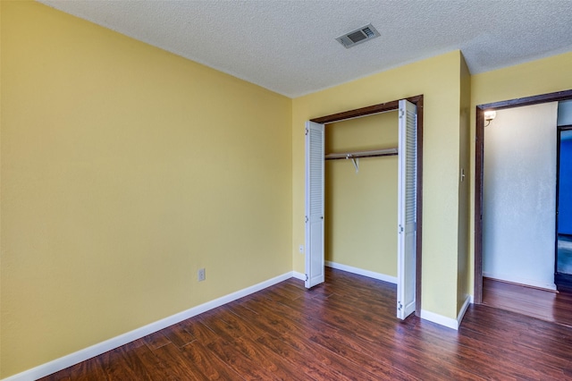 unfurnished bedroom featuring baseboards, visible vents, dark wood-style flooring, a textured ceiling, and a closet