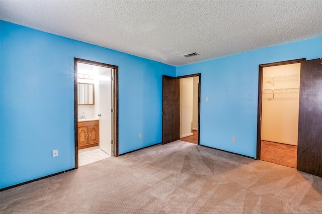 unfurnished bedroom with light carpet, visible vents, a walk in closet, and a textured ceiling