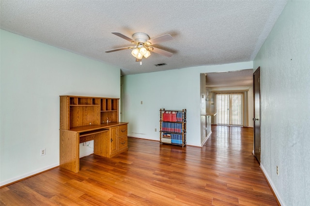 spare room featuring a textured ceiling, wood finished floors, visible vents, and a ceiling fan