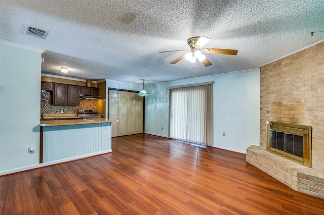 unfurnished living room with ornamental molding, a brick fireplace, wood finished floors, and visible vents