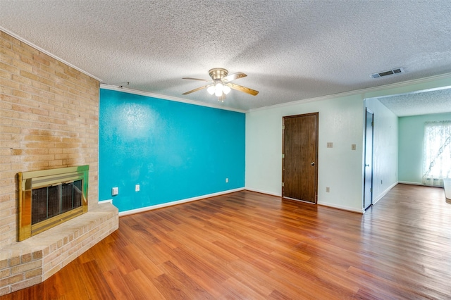 unfurnished living room with a brick fireplace, crown molding, visible vents, and wood finished floors