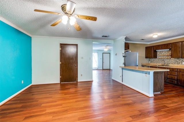 kitchen with a peninsula, wood finished floors, visible vents, light countertops, and freestanding refrigerator