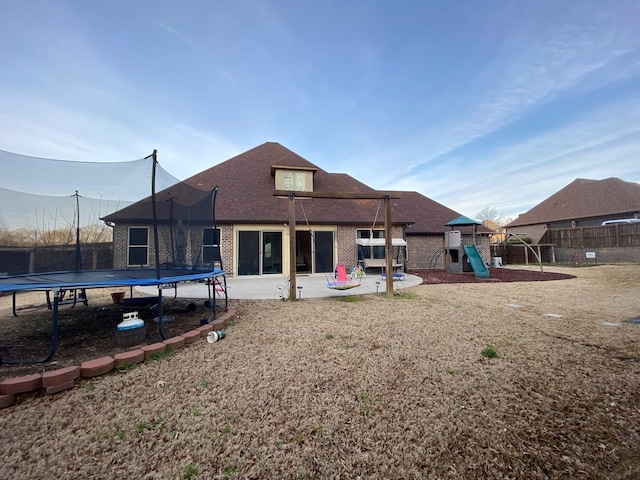 rear view of house with a patio, brick siding, a trampoline, and fence