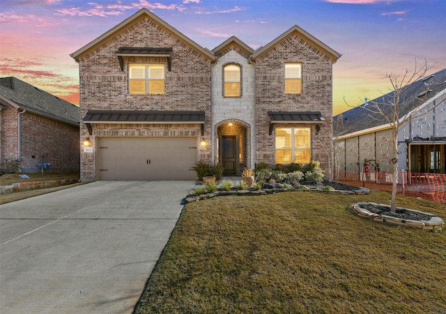 view of front of home featuring a garage, concrete driveway, stone siding, a yard, and brick siding