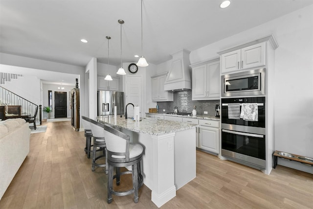 kitchen with premium range hood, appliances with stainless steel finishes, light wood finished floors, and decorative backsplash