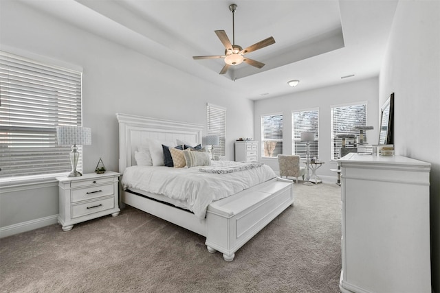 bedroom featuring a raised ceiling, light colored carpet, ceiling fan, and baseboards