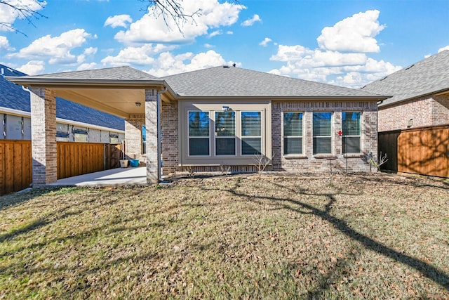 back of house with a shingled roof, a fenced backyard, a yard, a patio area, and brick siding