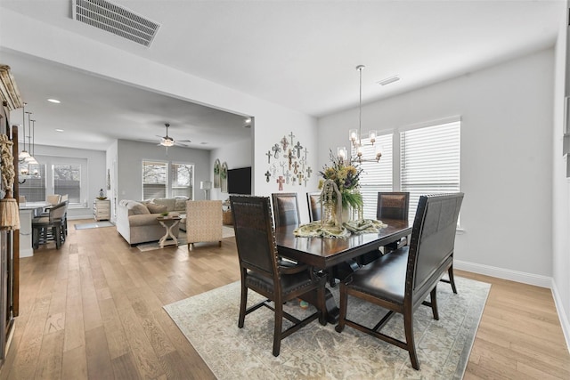 dining space featuring light wood-style flooring, visible vents, baseboards, and ceiling fan with notable chandelier