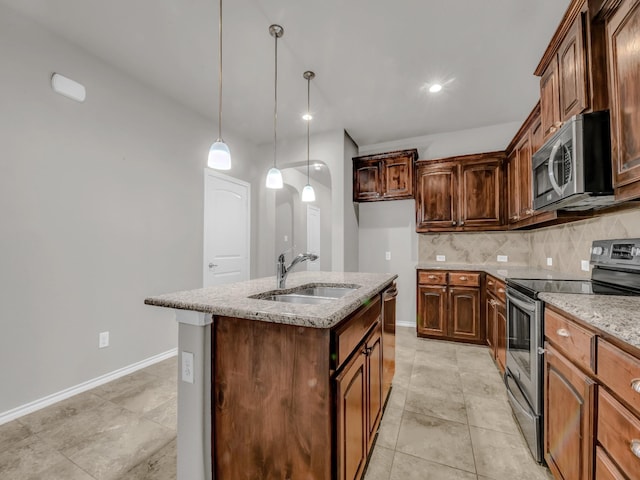 kitchen featuring light stone counters, a kitchen island with sink, a sink, appliances with stainless steel finishes, and tasteful backsplash