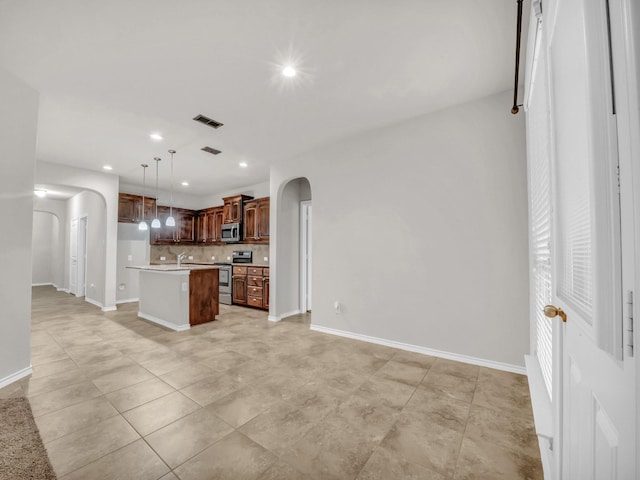 kitchen with arched walkways, stainless steel appliances, visible vents, light countertops, and tasteful backsplash