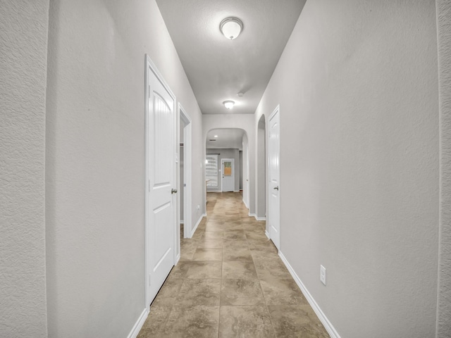 hallway featuring arched walkways, a textured wall, and baseboards