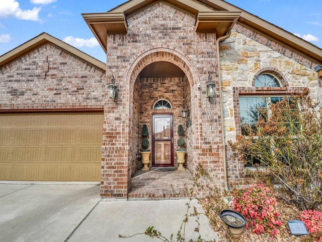 view of exterior entry with concrete driveway, brick siding, and an attached garage