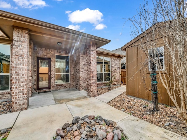 entrance to property with a patio area, fence, and brick siding