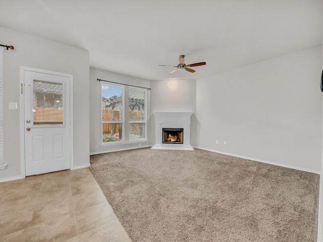 unfurnished living room featuring a warm lit fireplace, light carpet, ceiling fan, and baseboards