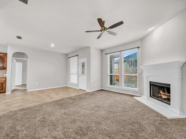 unfurnished living room featuring visible vents, arched walkways, light colored carpet, ceiling fan, and a lit fireplace