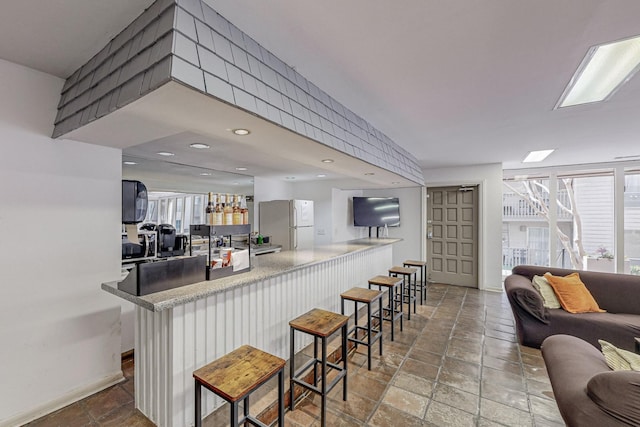 kitchen featuring baseboards, open floor plan, a kitchen breakfast bar, freestanding refrigerator, and stone finish flooring