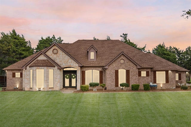 view of front of property featuring a shingled roof, french doors, brick siding, and a front lawn