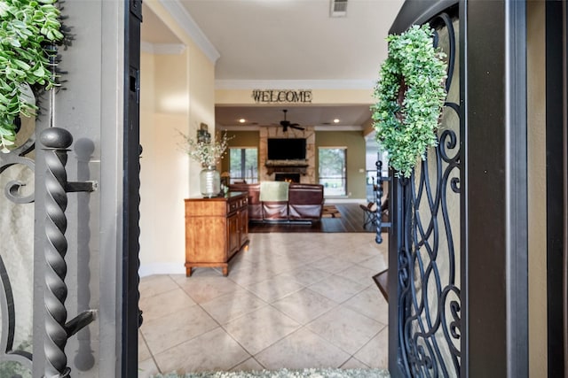 entrance foyer with crown molding, light tile patterned floors, visible vents, a lit fireplace, and baseboards