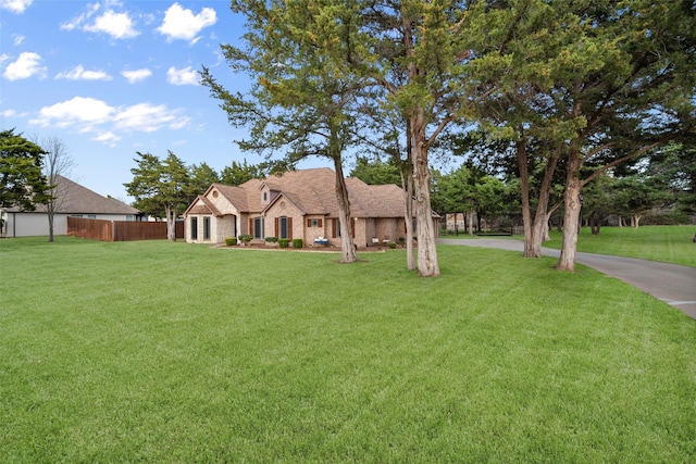 view of front of home with stone siding, a front lawn, and fence