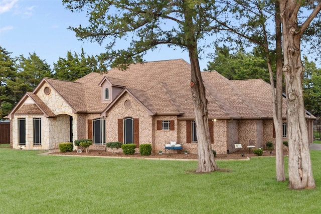 view of front of home featuring stone siding, a shingled roof, a front yard, and brick siding