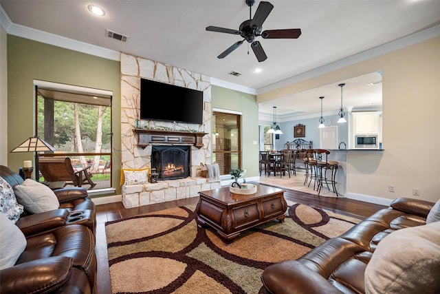 living room with a fireplace, visible vents, wood finished floors, and ornamental molding