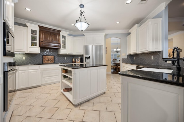 kitchen featuring arched walkways, stainless steel appliances, a sink, white cabinetry, and hanging light fixtures