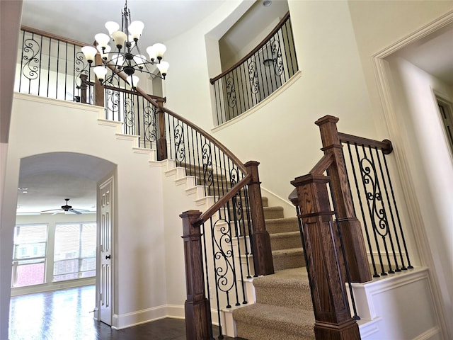 staircase with a high ceiling, ceiling fan with notable chandelier, baseboards, and arched walkways