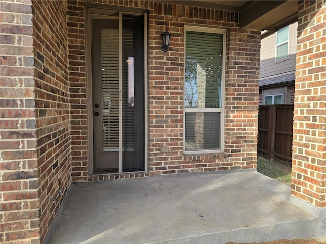 view of exterior entry featuring brick siding, a patio area, and fence