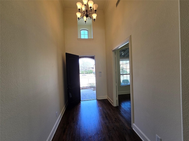 entryway with baseboards, dark wood-type flooring, an inviting chandelier, and ornamental molding