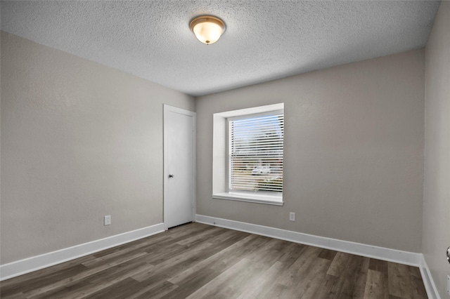 unfurnished room with dark wood-type flooring, a textured ceiling, and baseboards