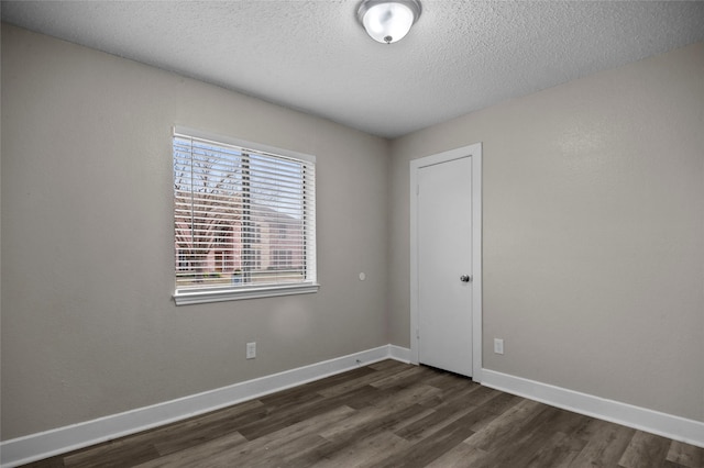 unfurnished room with dark wood-type flooring, a textured ceiling, and baseboards