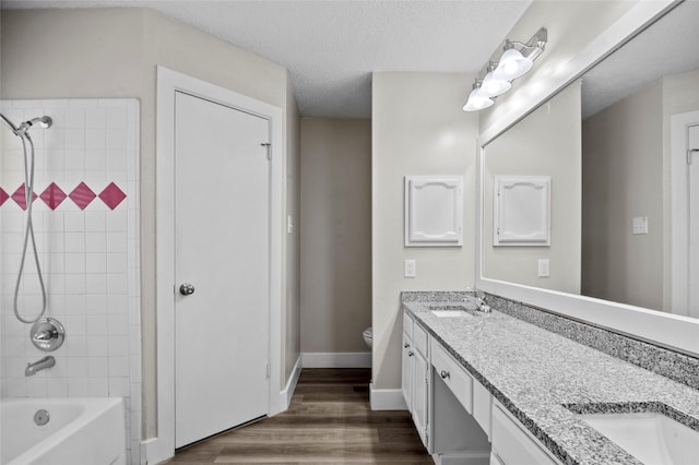 bathroom featuring double vanity, toilet, a sink, a textured ceiling, and wood finished floors