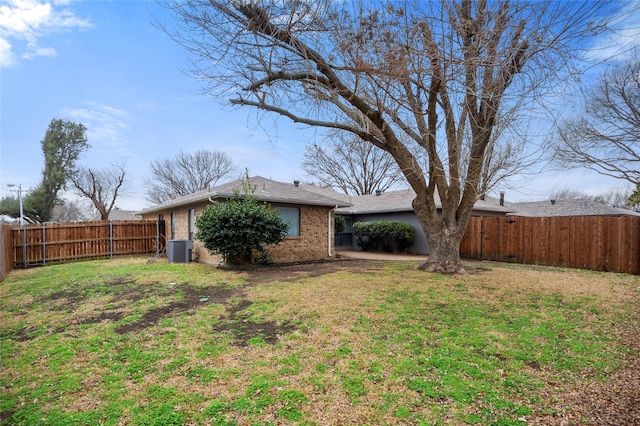 exterior space with a fenced backyard, a lawn, central AC, and brick siding