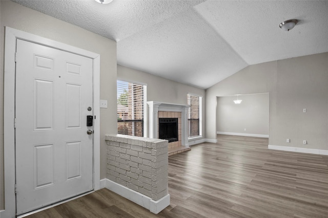 foyer entrance with baseboards, a tile fireplace, lofted ceiling, wood finished floors, and a textured ceiling