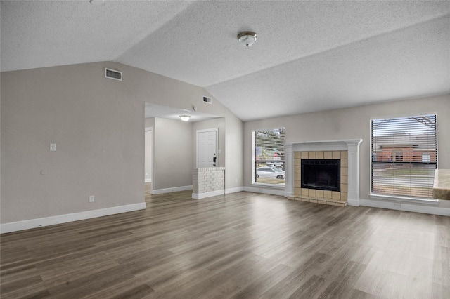 unfurnished living room featuring lofted ceiling, a tiled fireplace, wood finished floors, and visible vents