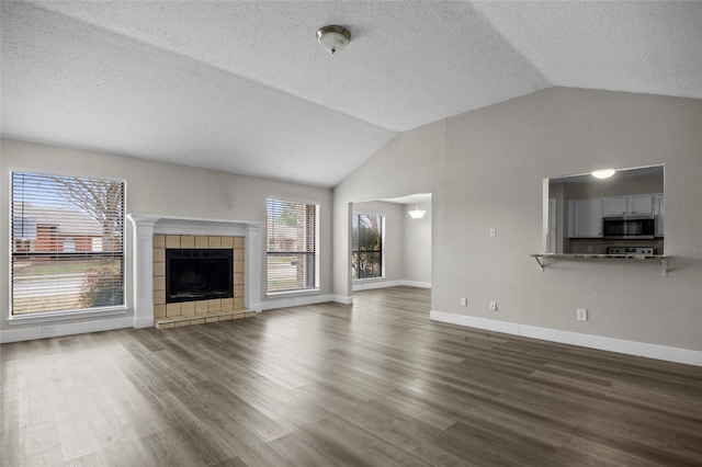 unfurnished living room with baseboards, vaulted ceiling, a tiled fireplace, and wood finished floors