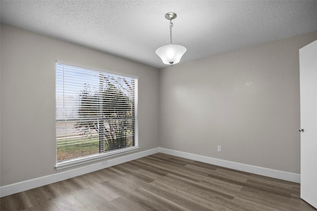 unfurnished room with a textured ceiling, baseboards, and wood finished floors