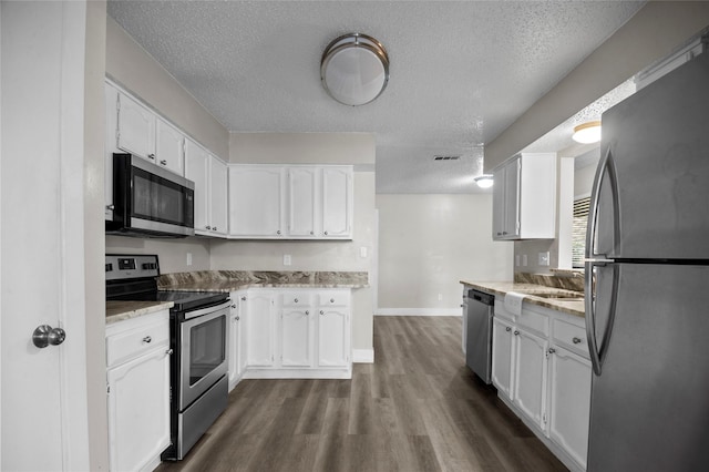 kitchen featuring light stone counters, dark wood finished floors, stainless steel appliances, white cabinetry, and a textured ceiling