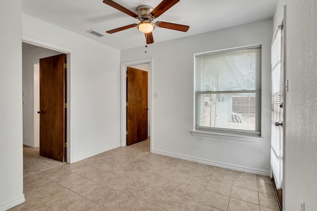 empty room featuring ceiling fan, light tile patterned floors, visible vents, and baseboards