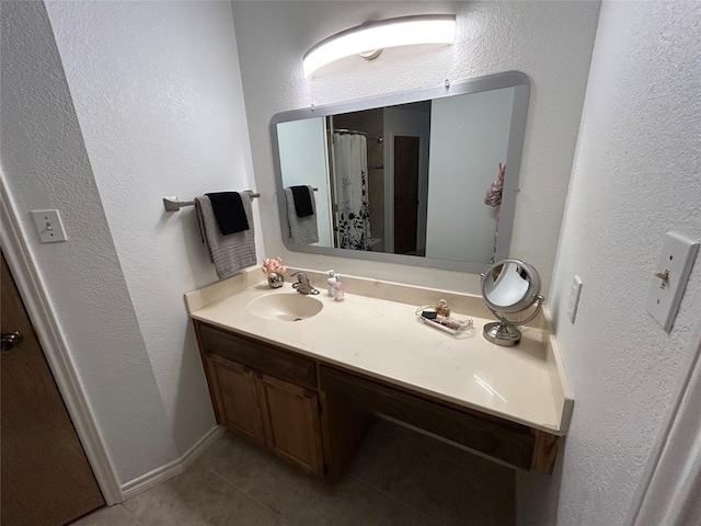 bathroom with a textured wall, vanity, baseboards, and tile patterned floors