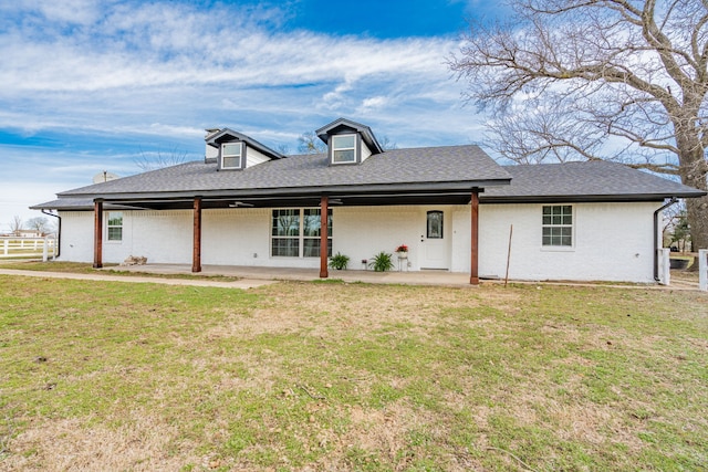 view of front of property featuring brick siding, roof with shingles, a front yard, a patio area, and fence