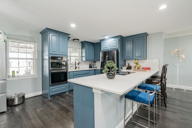 kitchen with stainless steel appliances, a peninsula, a breakfast bar, light countertops, and blue cabinetry