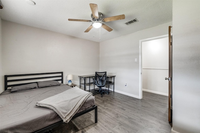 bedroom featuring baseboards, visible vents, a ceiling fan, wood finished floors, and a textured ceiling