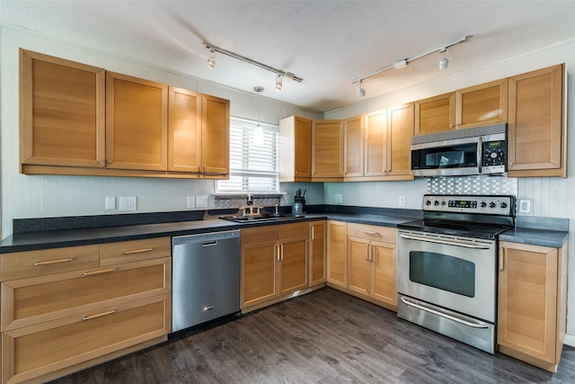 kitchen with a textured ceiling, stainless steel appliances, a sink, dark countertops, and dark wood finished floors