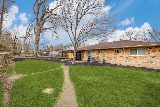 back of property featuring a shingled roof, a lawn, a fenced backyard, central air condition unit, and brick siding